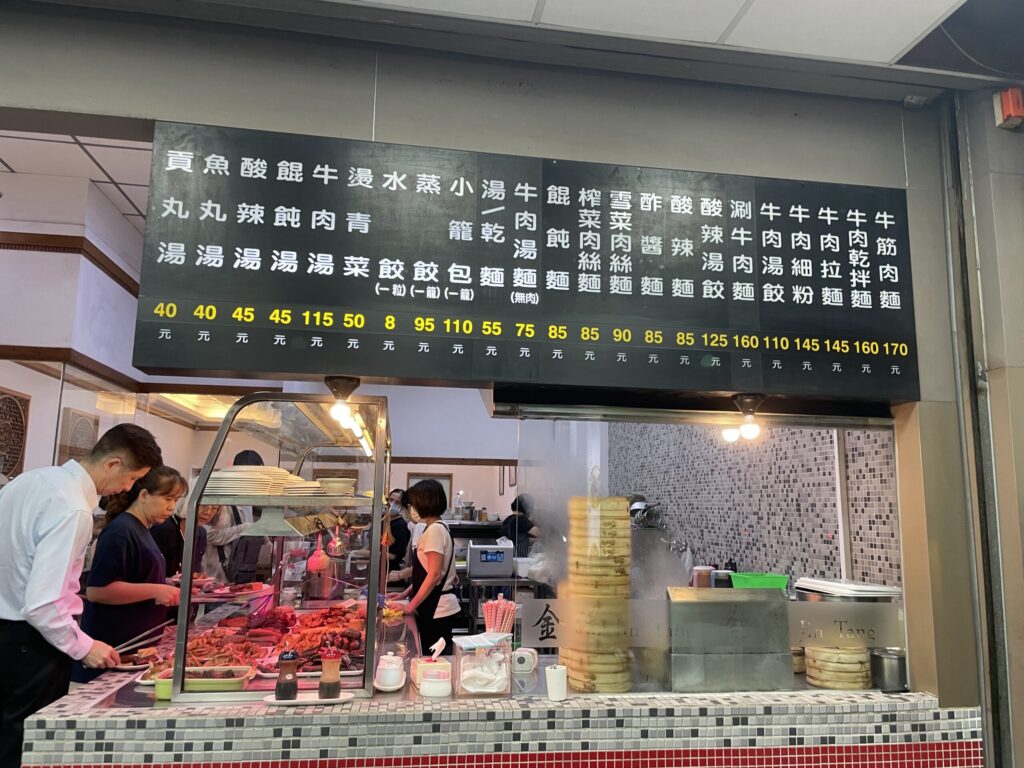 高雄の麺屋店先に並ぶ台湾式おでん（滷味）の具材とメニュー看板、店員が調理する様子を撮影