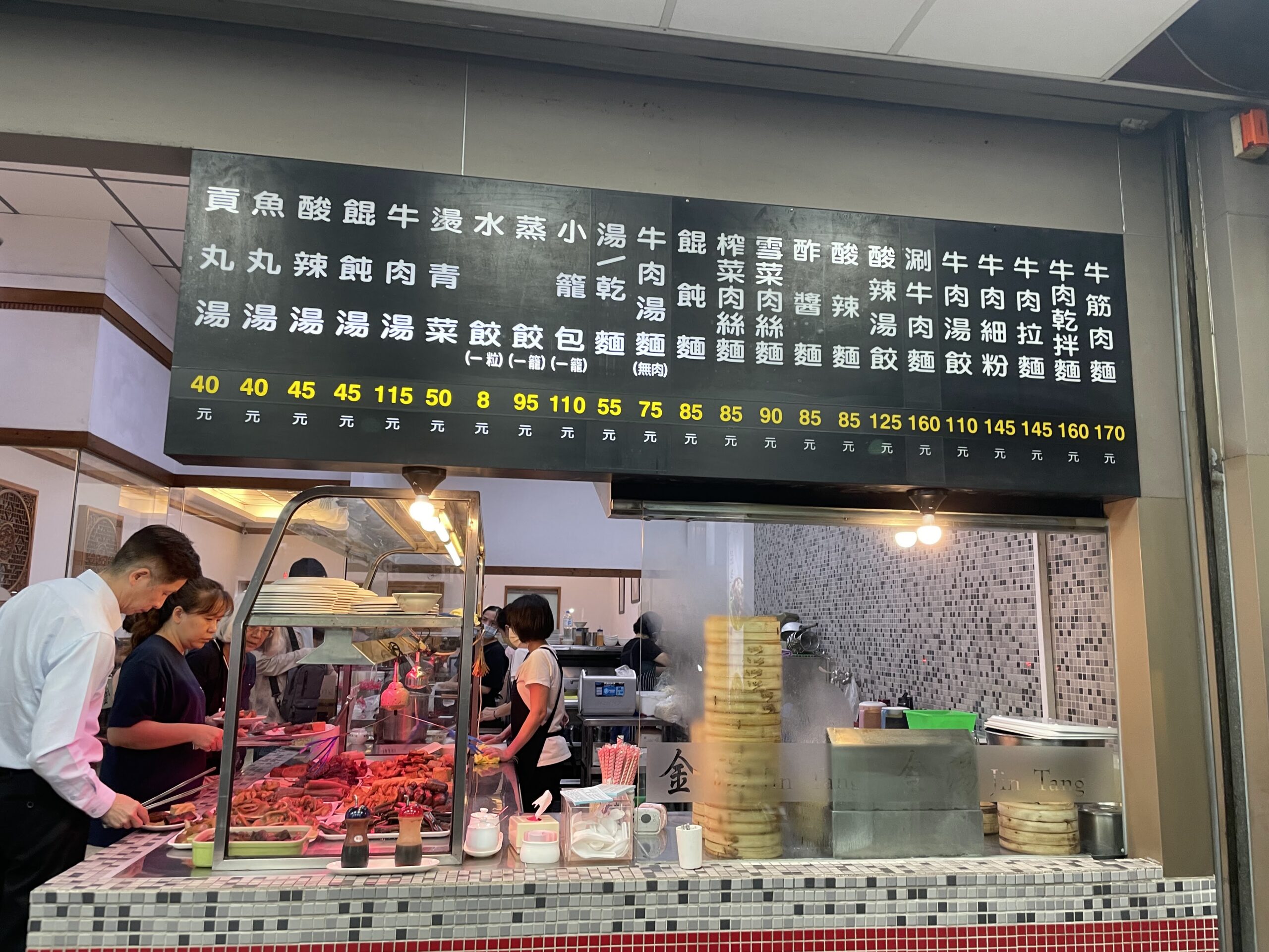 高雄の麺屋店先に並ぶ台湾式おでん(滷味)の具材とメニュー看板、店員が調理する様子を撮影