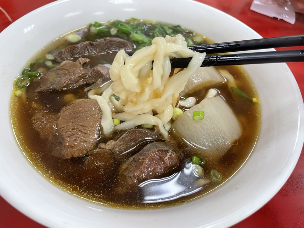 高雄 小籠包の名店で味わう原汁牛肉麺の麺をリフトした様子。ちぢれ麺ともちもち食感が伝わる一枚