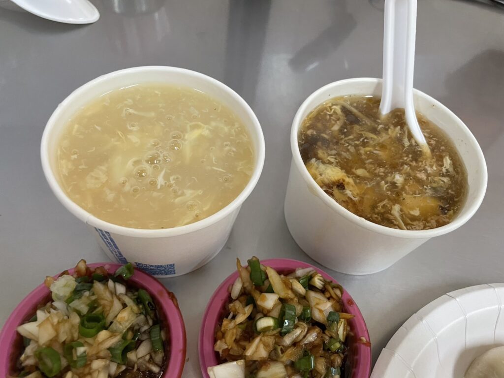 楠梓 小籠包の食堂で提供されるコーンスープと酸辣湯、手前には甘い醤油とねぎのみじん切りの薬味が山盛りに添えられている