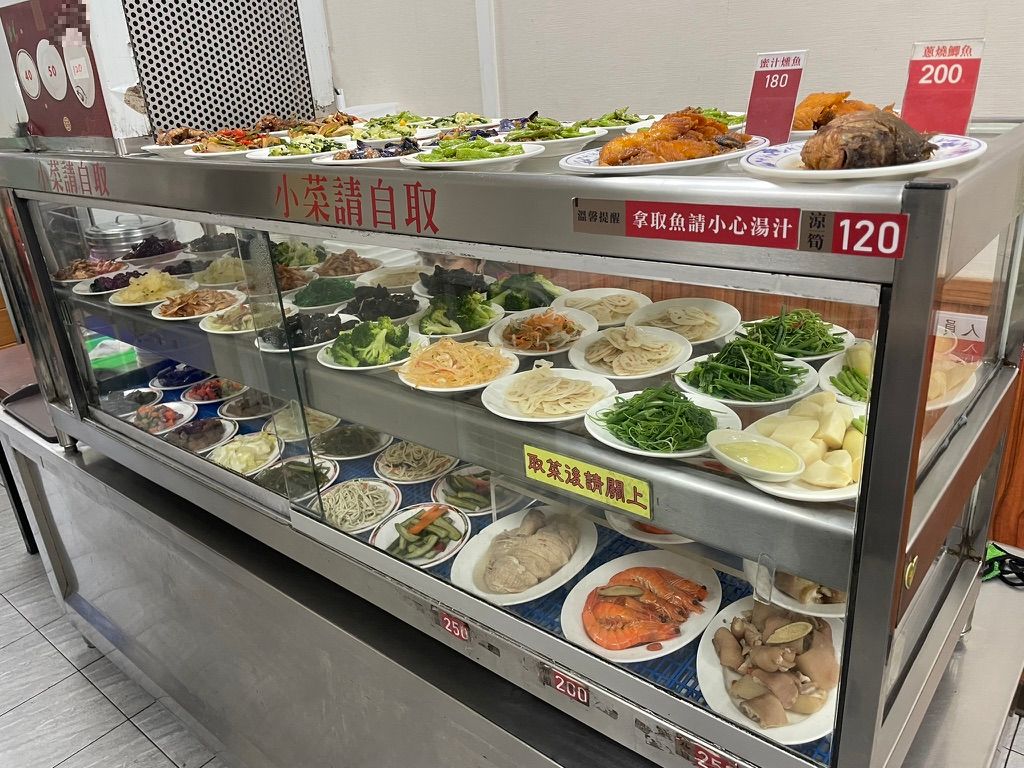 高雄 小籠包の店内にあるおかずのセルフサービスコーナー。小皿に盛られた野菜や副菜が並ぶ