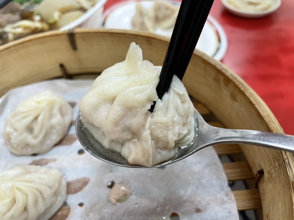 高雄 小籠包の名店で鮮肉湯包を箸でつまむと肉汁がとろりと溢れ出る様子（Kaohsiung Xiao Long Bao）